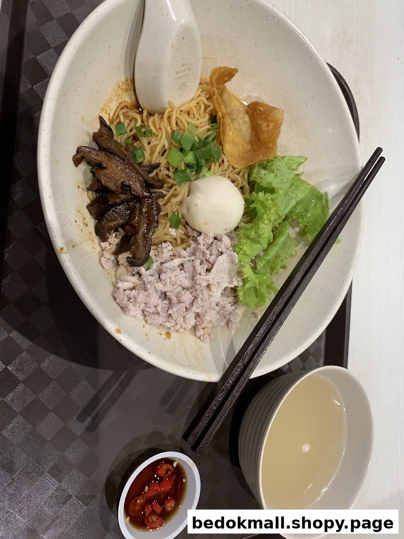 A bowl of noodles with various toppings, chopsticks, and a side of soup.