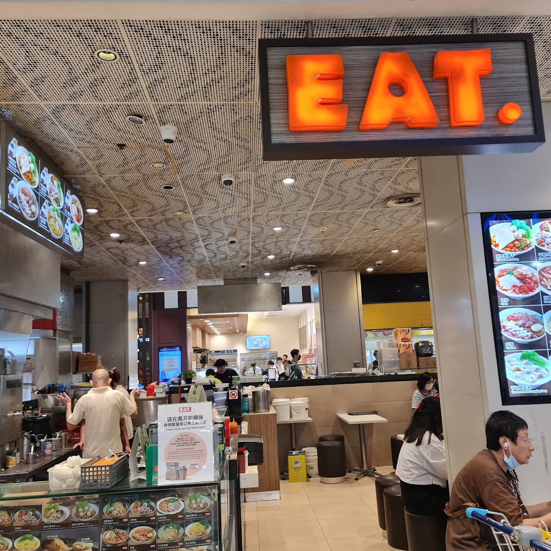 A busy food stall interior with staff, customers, and food displays.