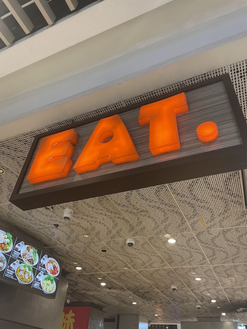 Large illuminated 'EAT.' sign above a menu board in a shop interior.
