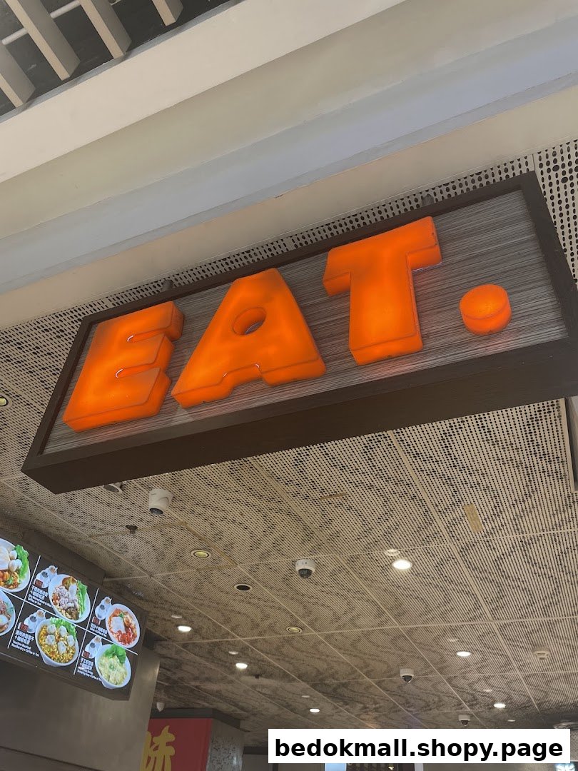 Large illuminated 'EAT.' sign above a menu board in a shop interior.
