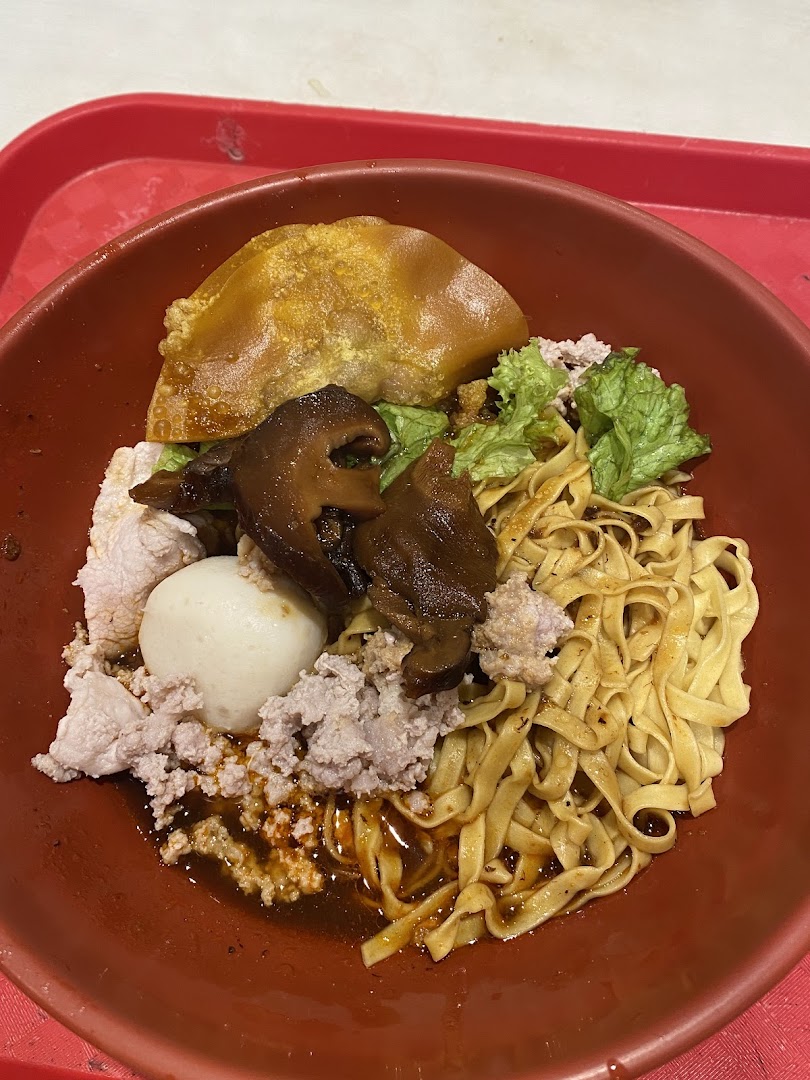 A bowl of noodles with minced meat, mushrooms, and a fried dumpling.