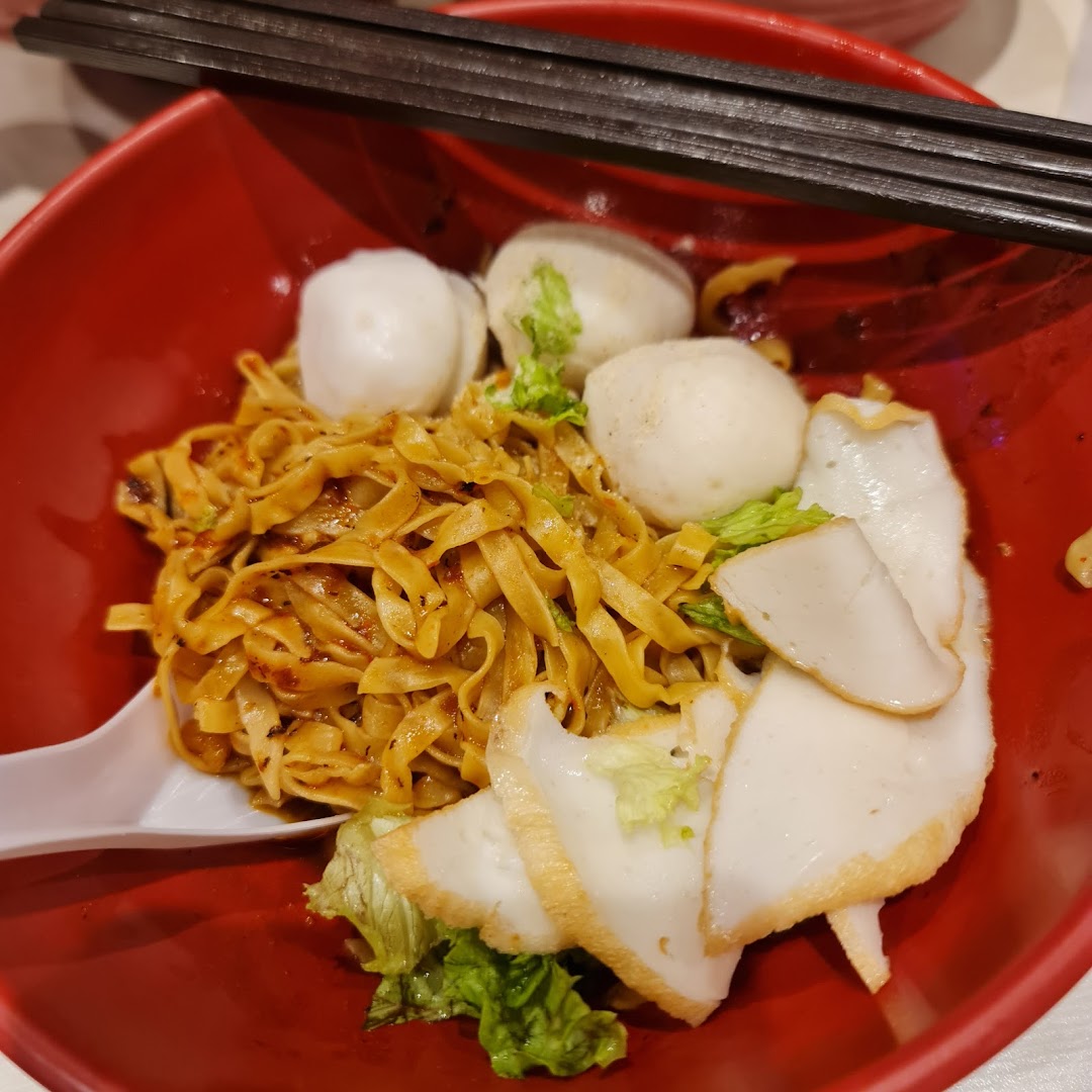 Close-up of noodles with fish balls and fish cake in a red bowl.