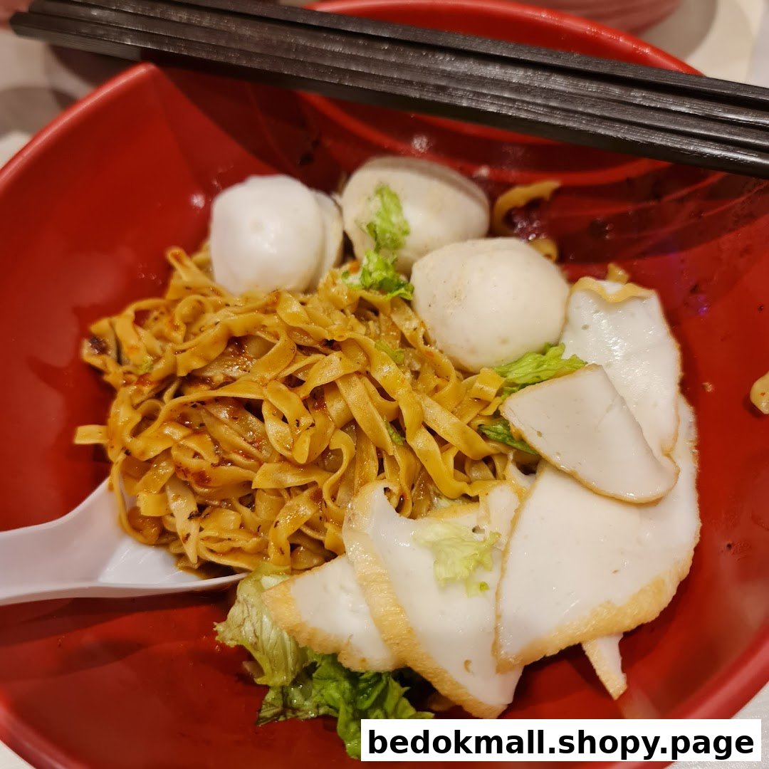 Close-up of noodles with fish balls and fish cake in a red bowl.