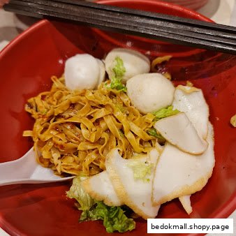 A red bowl of noodles with fish balls and fish cake.