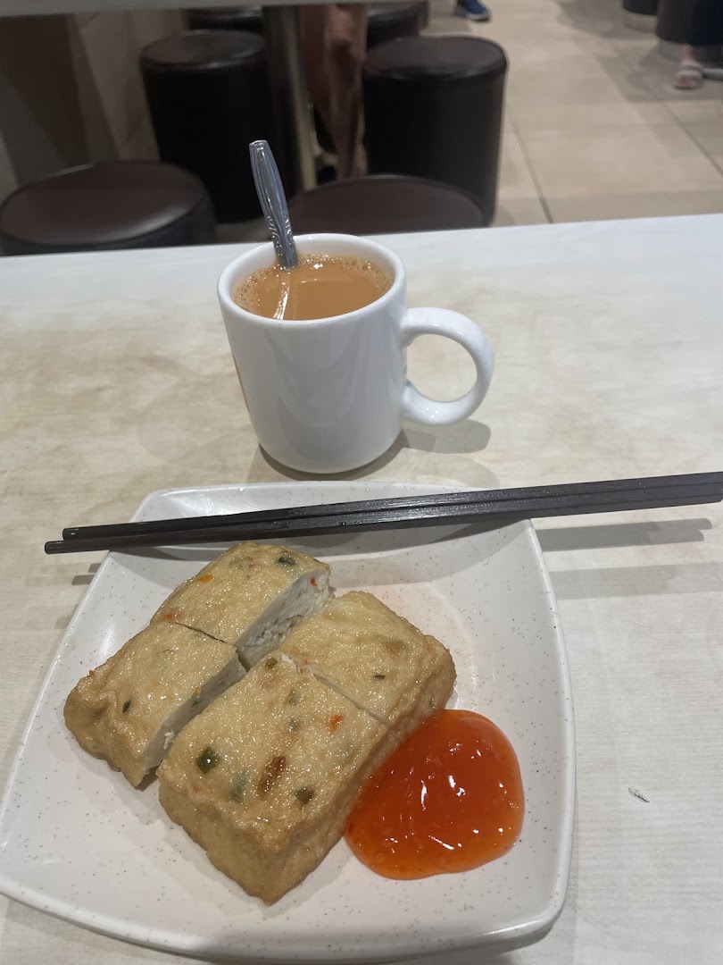 Plate of food with sauce, chopsticks, and a cup of beverage on a table.