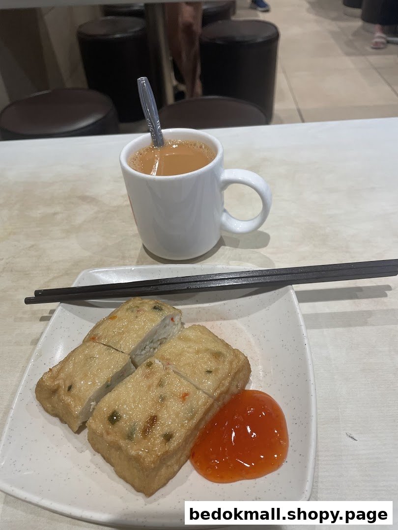 Plate of food with sauce, chopsticks, and a cup of beverage on a table.