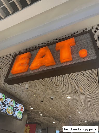 Illuminated 'EAT.' sign above a menu board in a food establishment.
