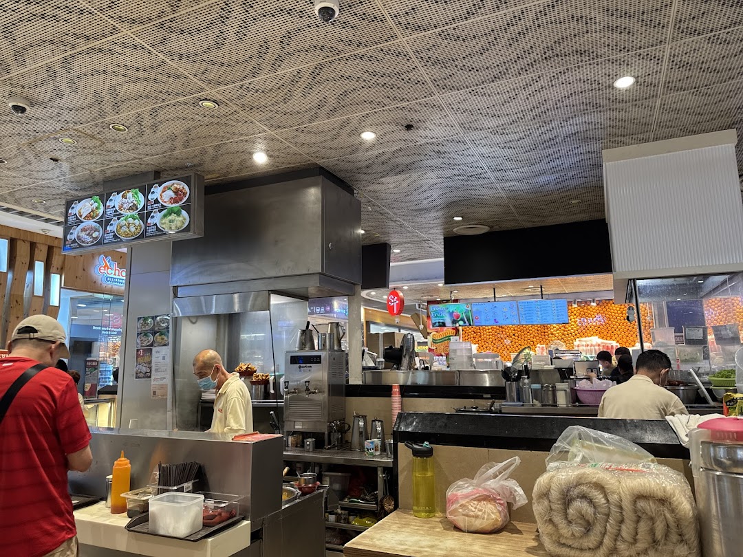 Busy food stall interior with staff, customers, and food preparation.
