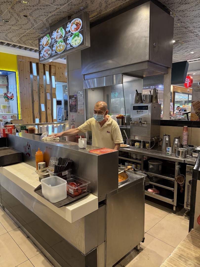 Staff member working at a food stall counter with a menu board above.
