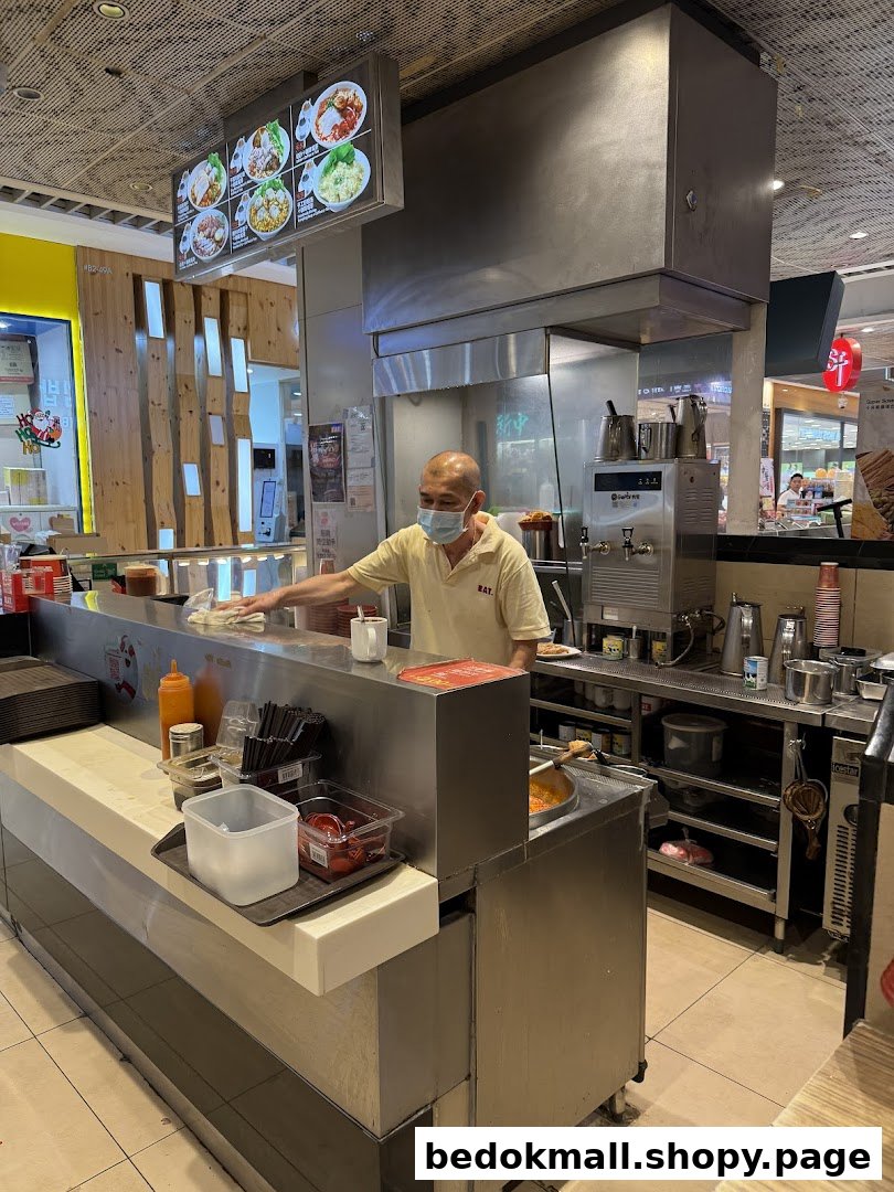 Staff member working at a food stall counter with a menu board above.