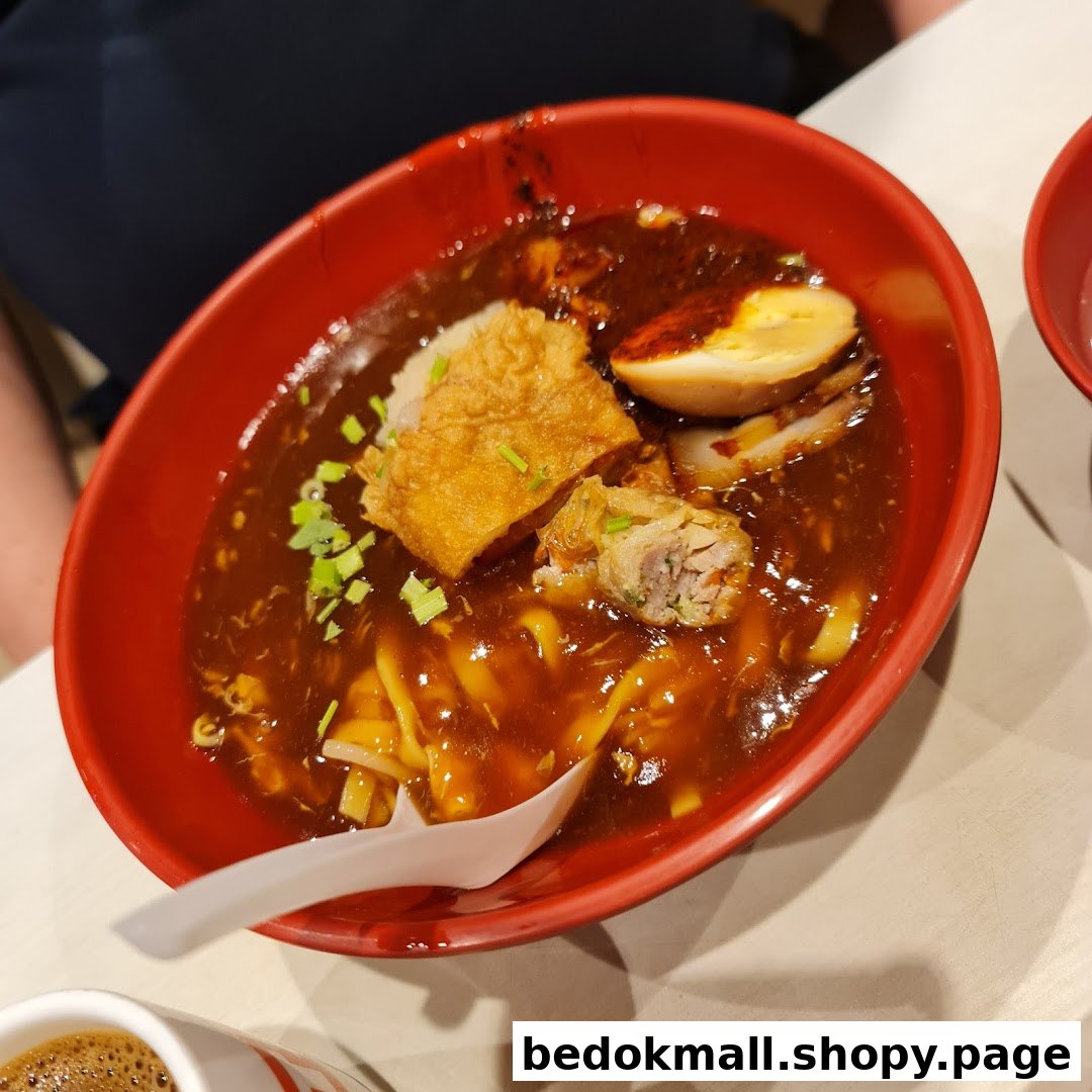 A red bowl of noodles with dark sauce, egg, and fried toppings.