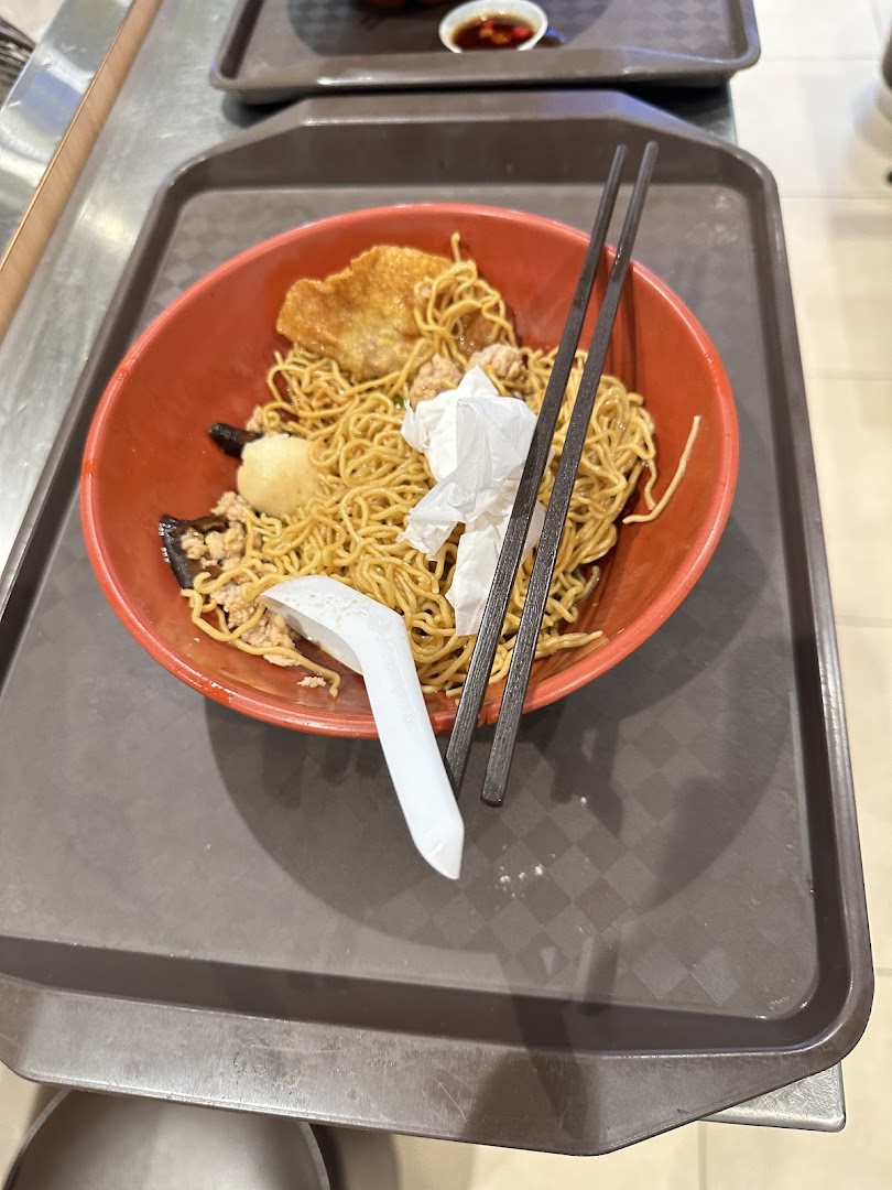 A bowl of noodles with chopsticks and a spoon on a brown tray.
