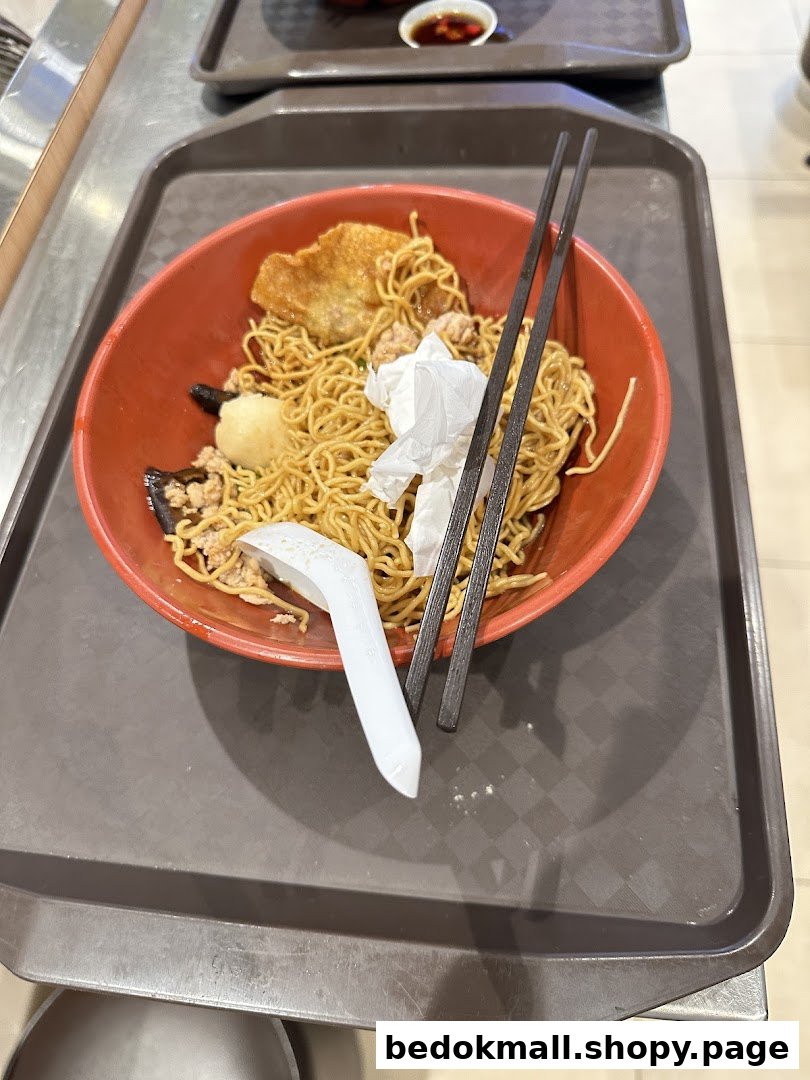 A bowl of noodles with chopsticks and a spoon on a brown tray.