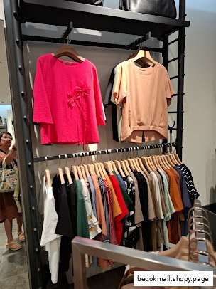 Clothing on display racks inside a retail shop with a person in the background.