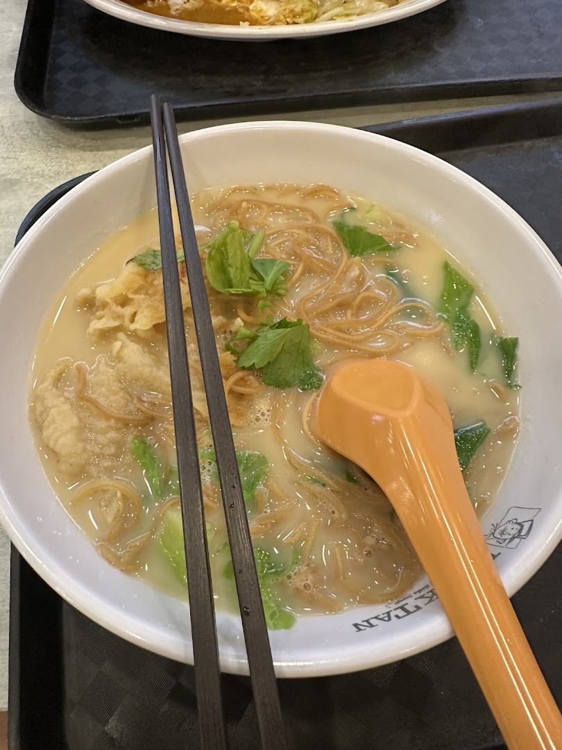 A bowl of noodles with broth, vegetables, chopsticks, and a spoon.