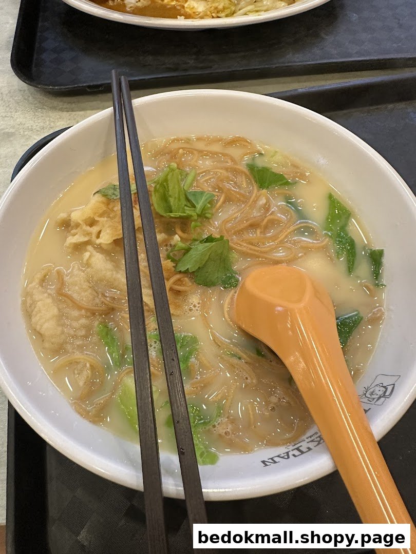 A bowl of noodles with broth, vegetables, chopsticks, and a spoon.