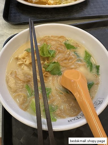 A close-up of a bowl of noodles with chopsticks and a spoon.
