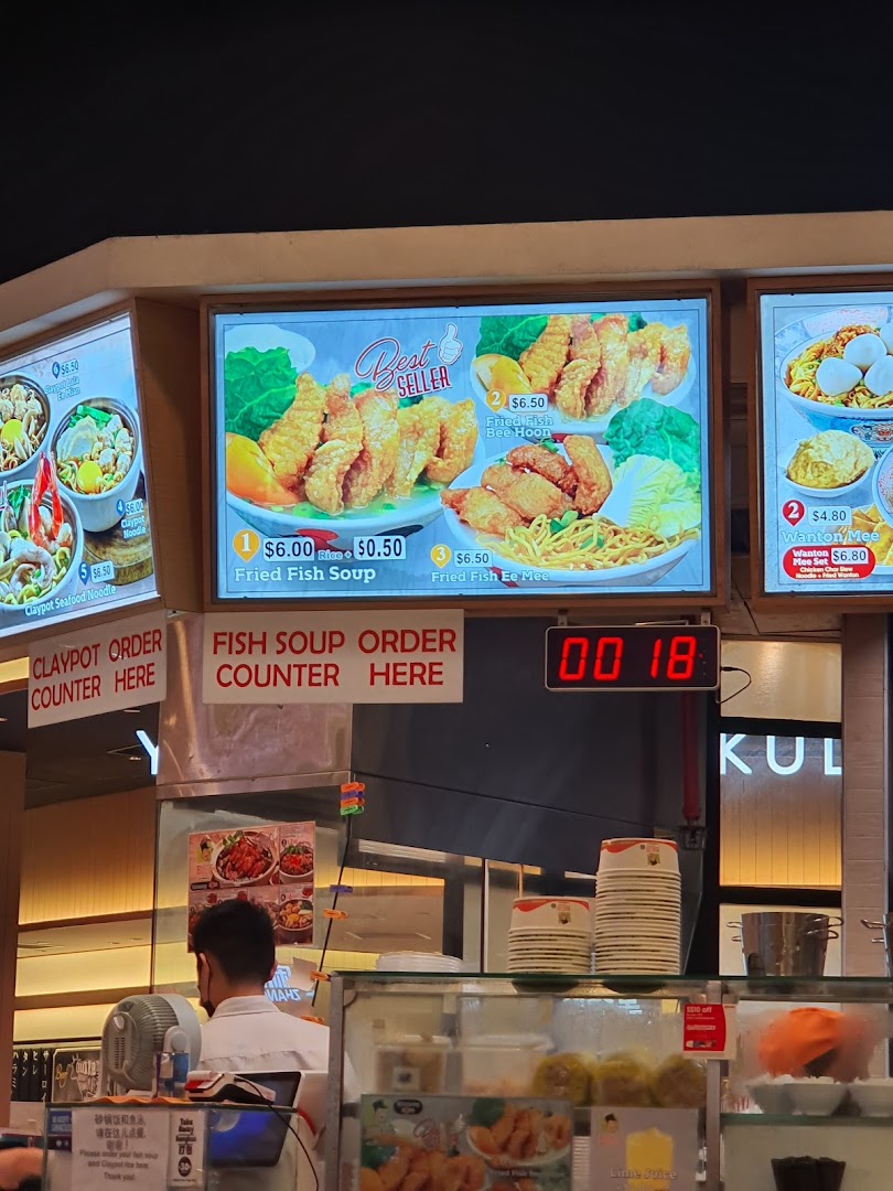 Interior view of a food stall counter with digital menus and a staff member.