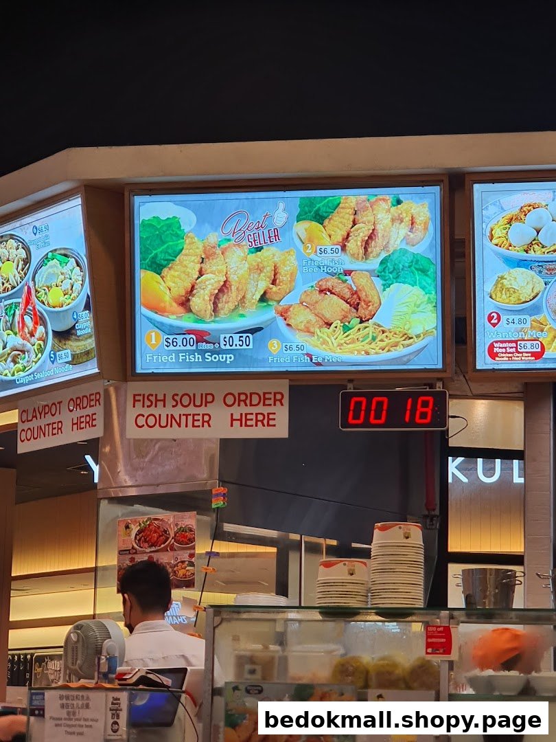Interior view of a food stall counter with digital menus and a staff member.