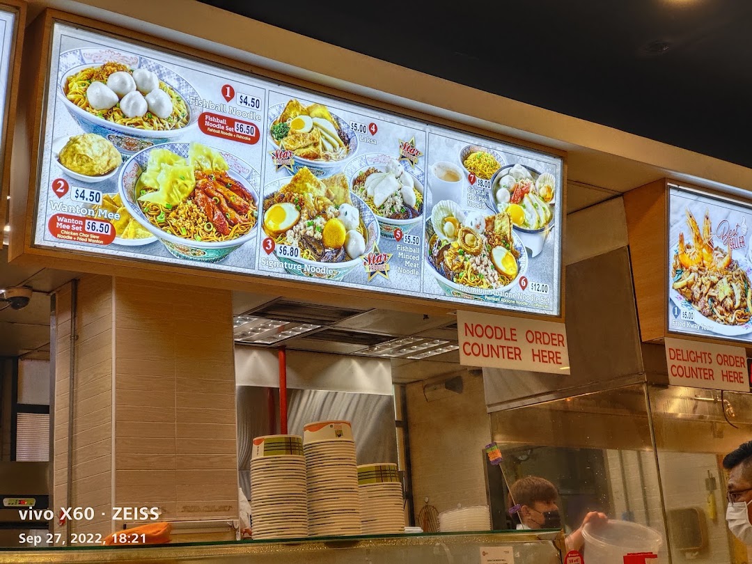 Illuminated menu boards display various noodle dishes and prices above a food counter.