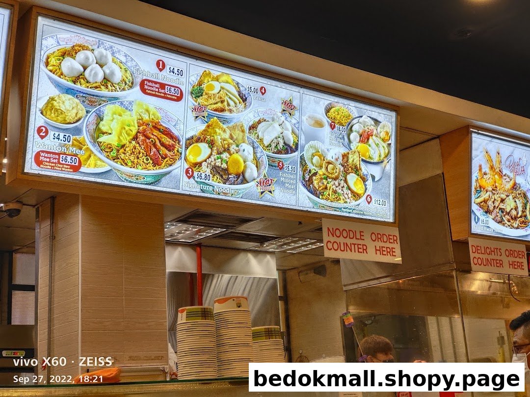 Illuminated menu boards display various noodle dishes and prices above a food counter.