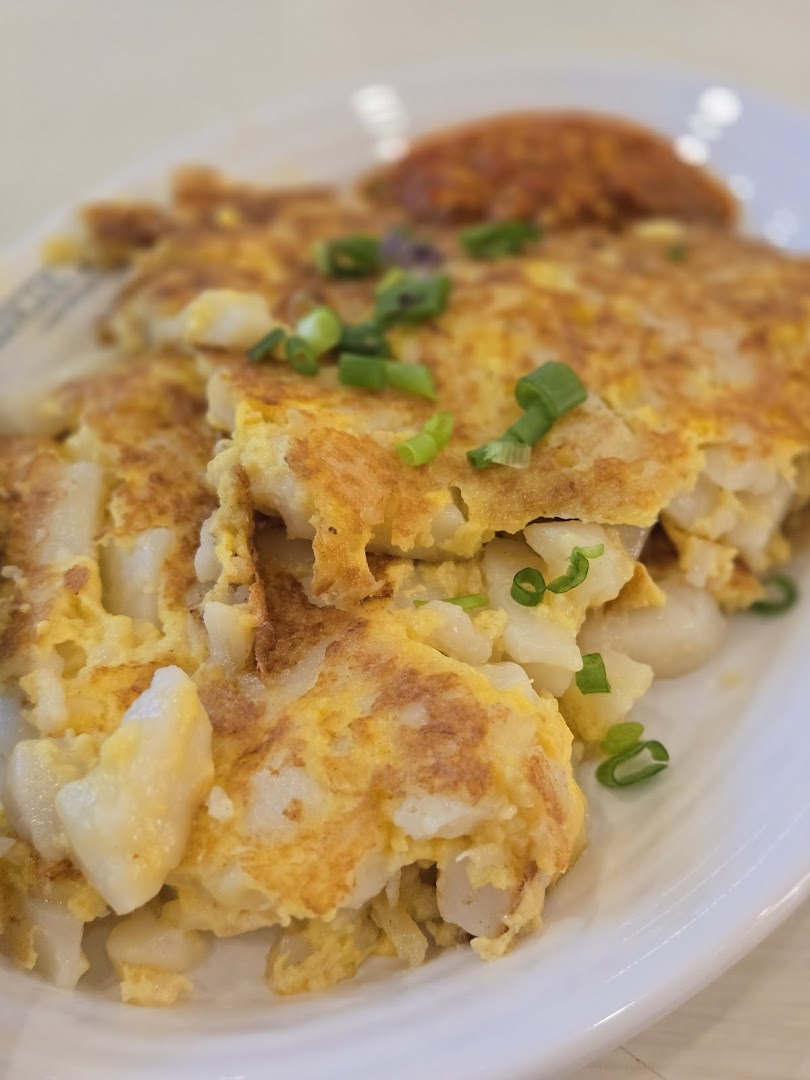 Close-up of a plate of fried radish cake with egg and green onions.