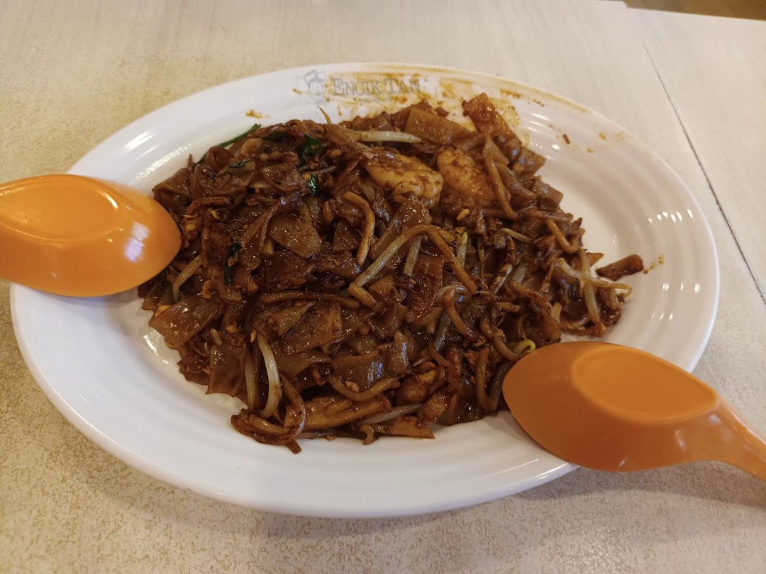 A plate of dark fried noodles with two orange spoons.