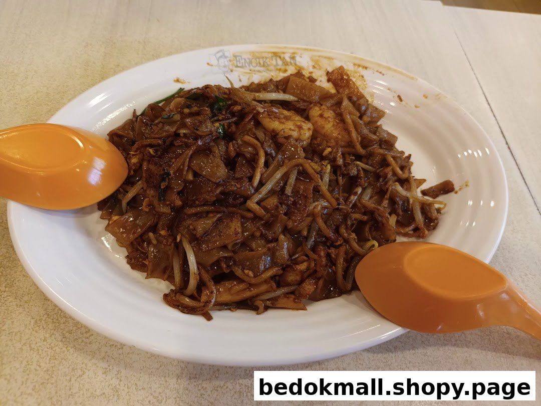A plate of dark fried noodles with two orange spoons.