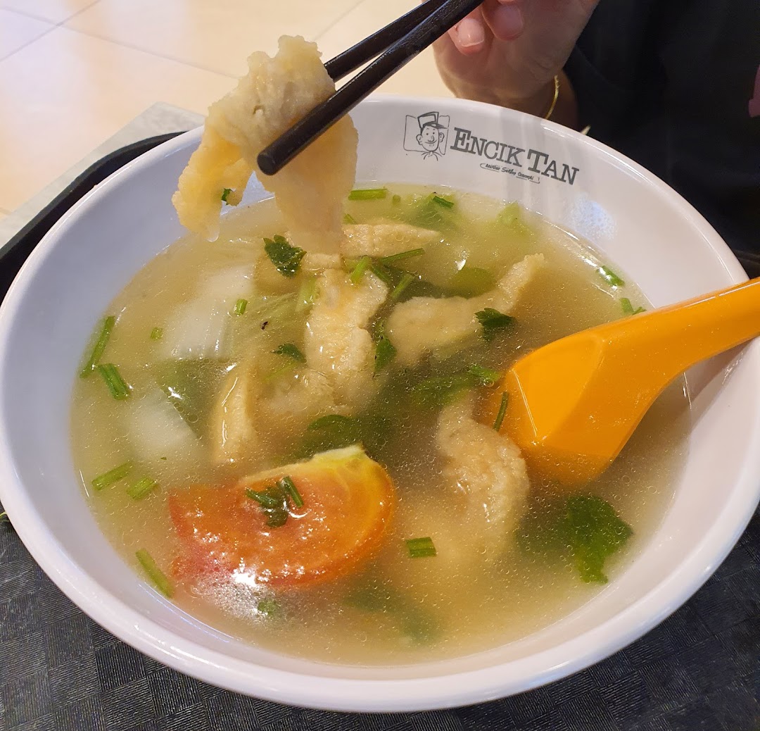 A bowl of soup with food being picked up by chopsticks.