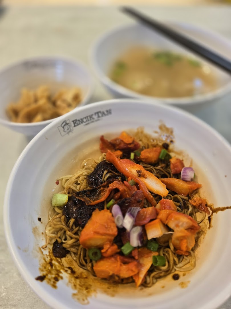 A close-up of a bowl of noodles with other food items on a table.