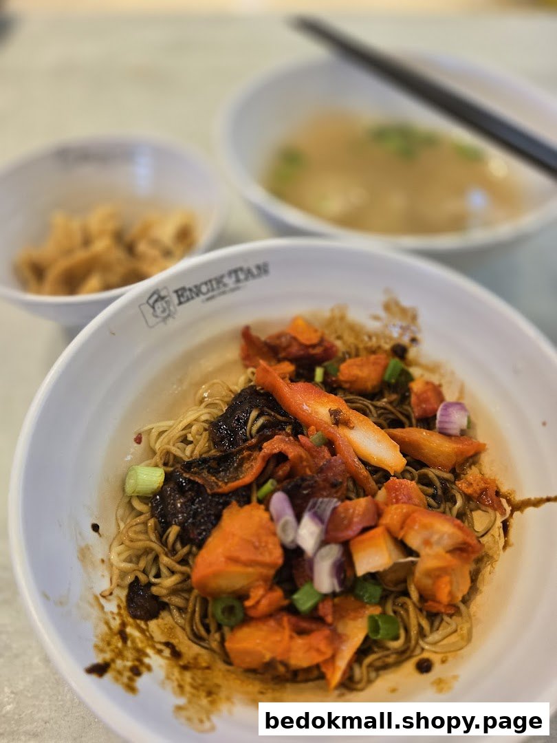 A close-up of a bowl of noodles with other food items on a table.
