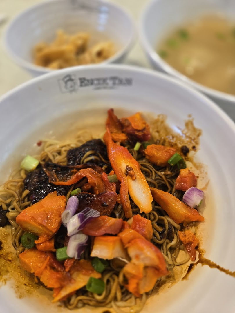 Close-up of a bowl of dark sauced noodles with chicken and onions.