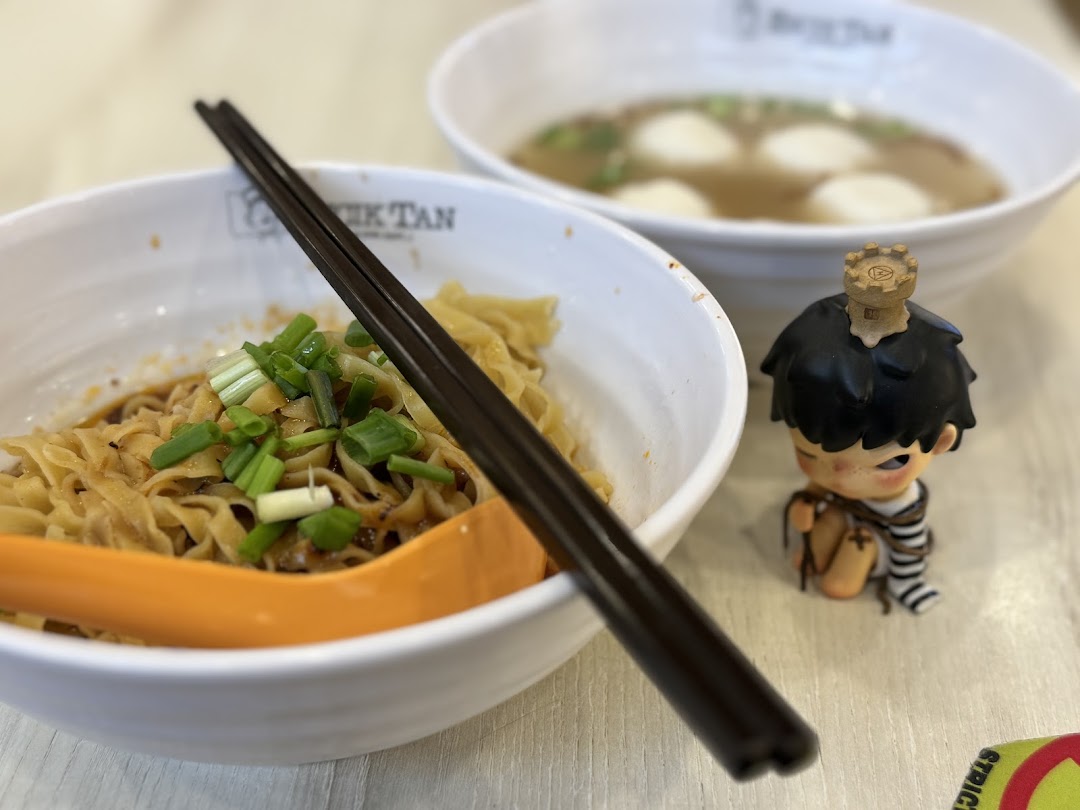 Two bowls of noodles and soup with a small figurine on a table.