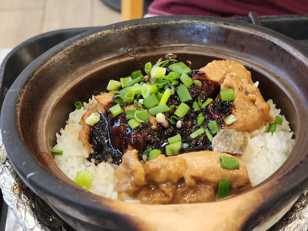 Close-up of claypot rice with chicken, dark sauce, and green onions.