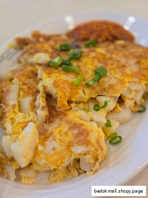 Close-up of fried radish cake with egg and green onions on a white plate.