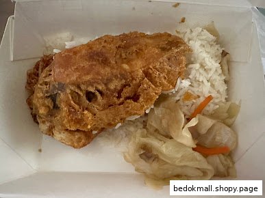 Fried chicken cutlet with rice and vegetables in a takeaway box.
