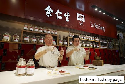 Two staff members weigh ingredients behind a counter in a traditional Chinese medicine shop.