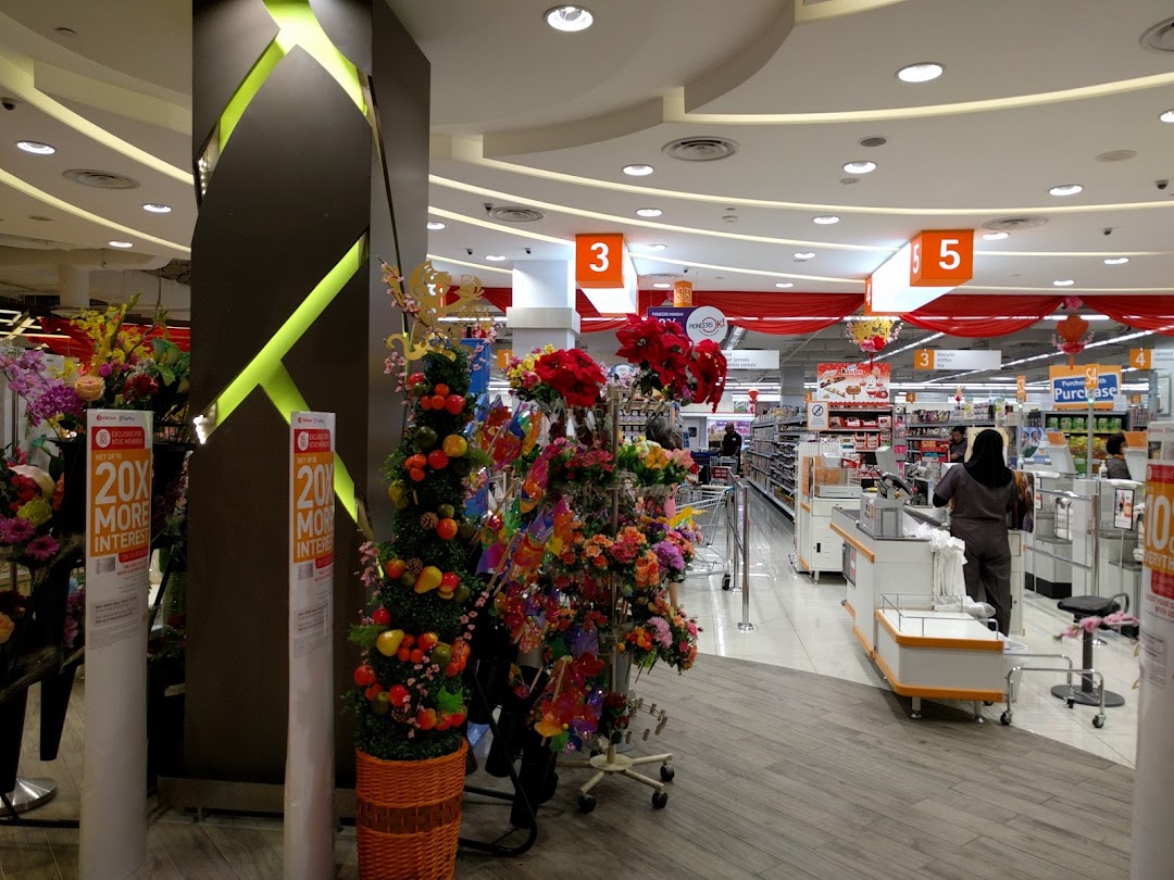 Interior view of a supermarket with checkout counters, staff, and decorative plants.