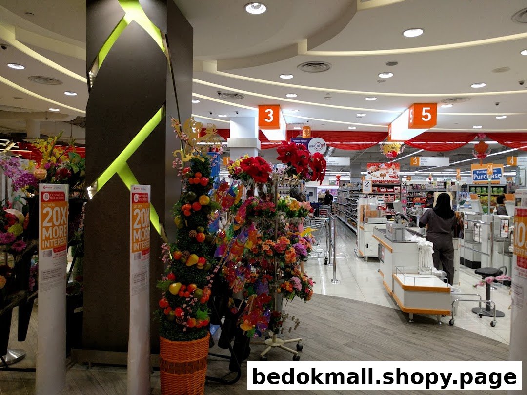 Interior view of a supermarket with checkout counters, staff, and decorative plants.