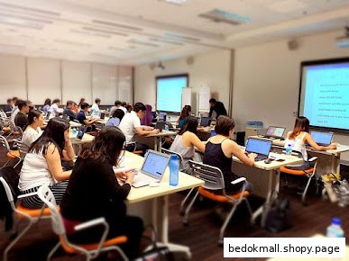 People are in a classroom setting, working on laptops with projected screens.