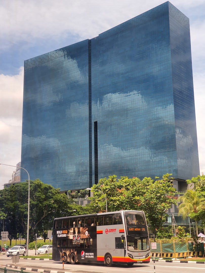 A large glass building, a double-decker bus, and trees on a street.