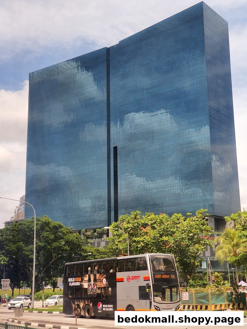 A large glass building, a double-decker bus, and trees on a street.