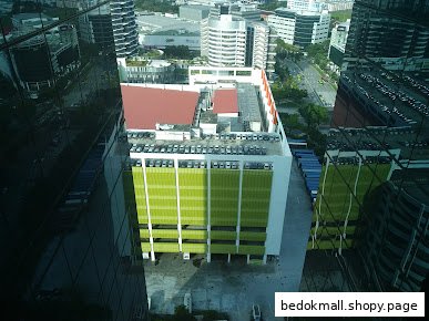 High-angle view of a multi-story building with green facade and rooftop parking.
