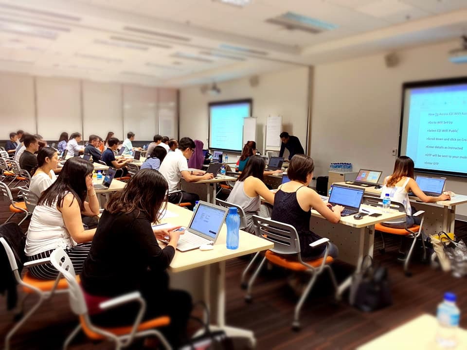 People in a classroom setting using laptops with projected screens.