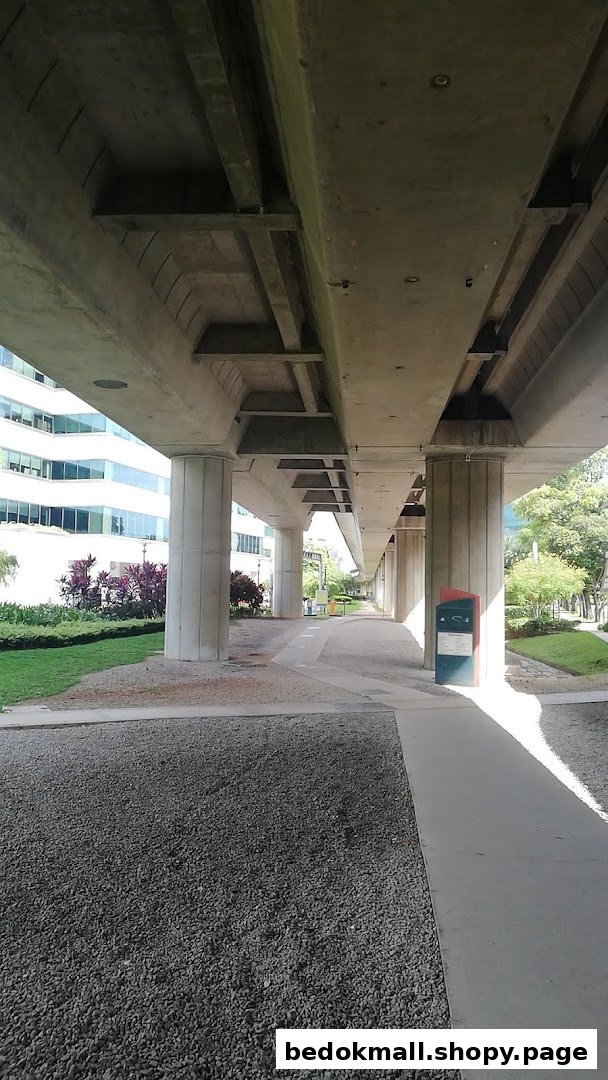 View under an elevated concrete structure with pillars, gravel, and a walkway.