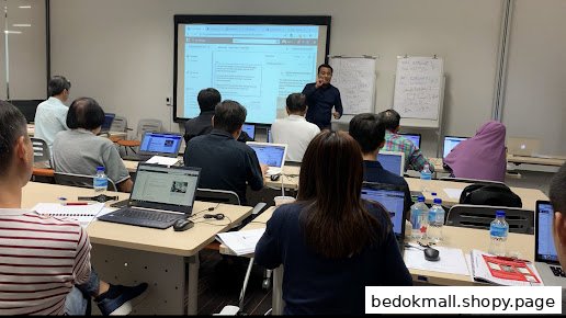 People attending a training session in a classroom with a speaker and laptops.