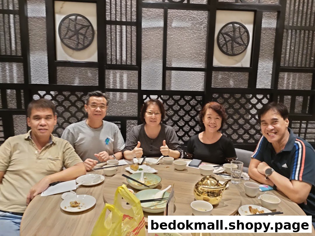 Five people are seated around a round table, dining in a restaurant.