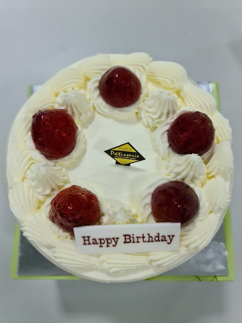 A white cake topped with strawberries, whipped cream, and a 'Happy Birthday' plaque.