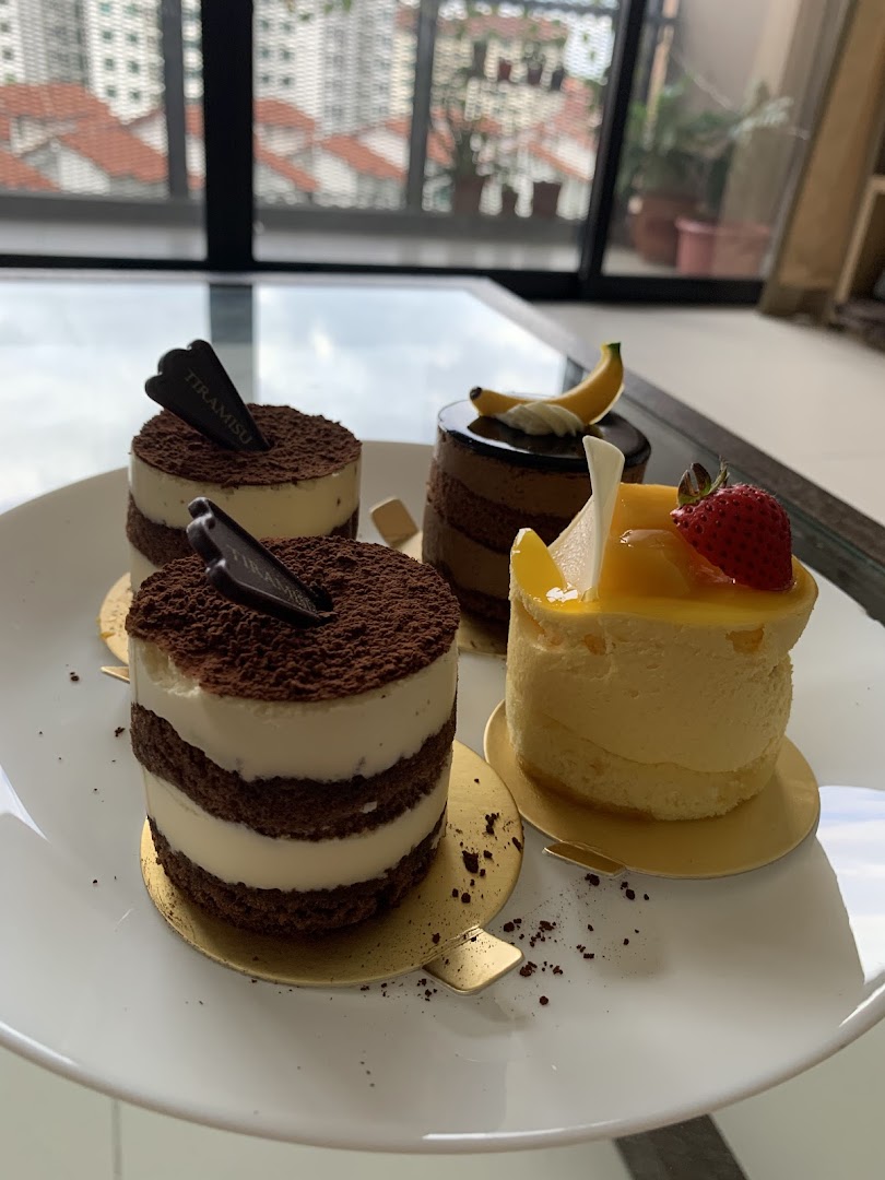 Four small cakes, including tiramisu and fruit, on a white plate.
