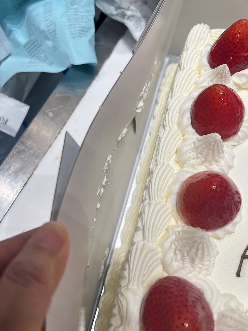 Close-up of a strawberry cake in a box, held by a hand.